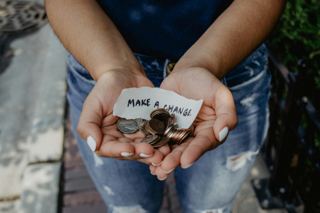 Cupped hands holding coins with a handwritten note reading MAKE A CHANGE